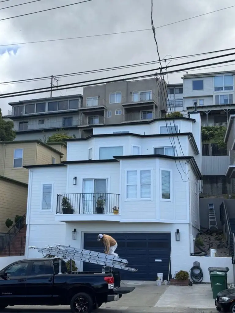 White three-story hillside home with dark garage doors, exterior repaint by Wilmar's Painting