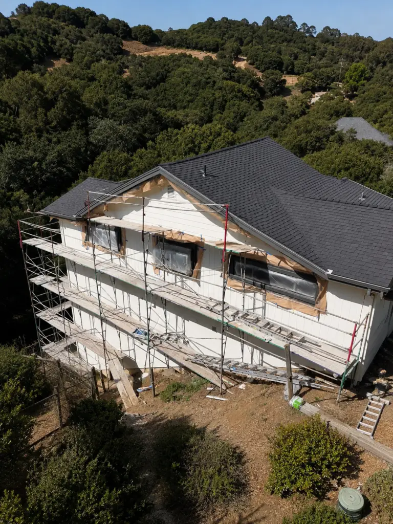 Aerial view of a large hillside home mid-repaint with scaffolding and new siding, prep work by Wilmar's Painting