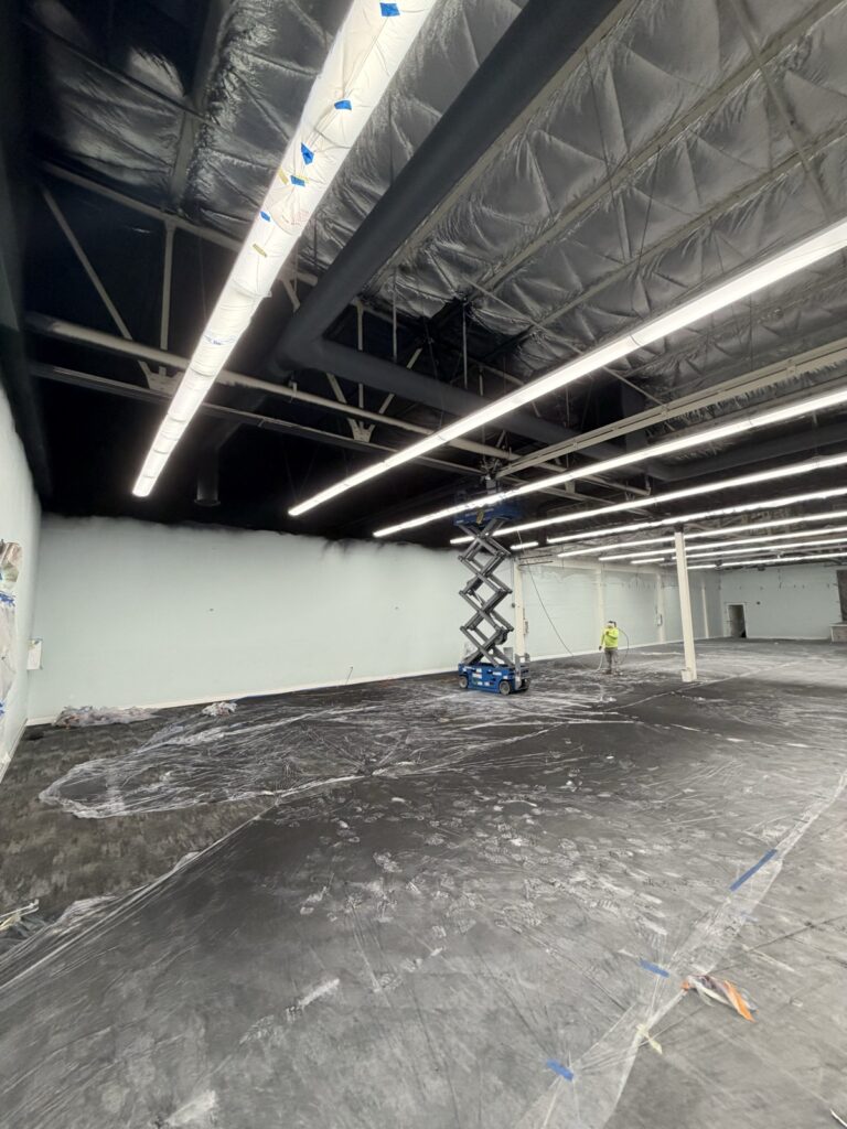 Commercial warehouse ceiling being spray-painted from a scissor lift by Wilmar's Painting