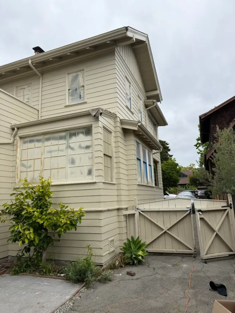 Cream-colored house exterior being prepped for painting, windows taped, by Wilmar's Painting